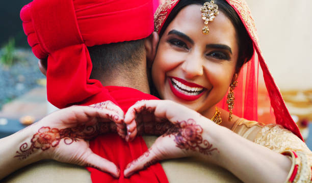 I gave him my heart for keeps Shot of a happy young woman hugging her husband and making a heart gesture on their wedding day indian bride stock pictures, royalty-free photos & images