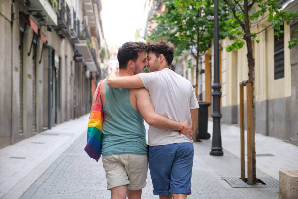 Gay couple about to kiss while walking and hugging in the street backwards. stock photo