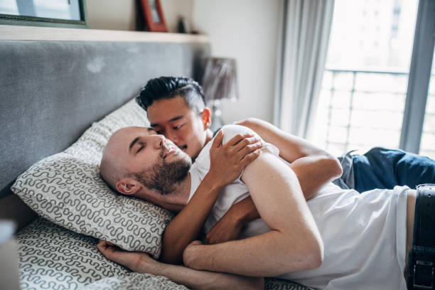 Gay couple Young multi-ethnic guy couple laying in bed in their bedroom. gay spooning stock pictures, royalty-free photos & images