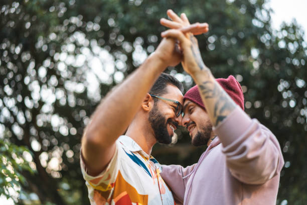 гей пара касаясь рук в общественном парке - lgbtq стоковые фото и изображения