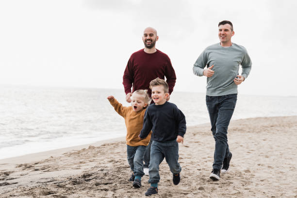 Gay family having fun together on the beach in summer vacation - LGBT dads and sons lifestyle concept - Main focus on right man face stock photo