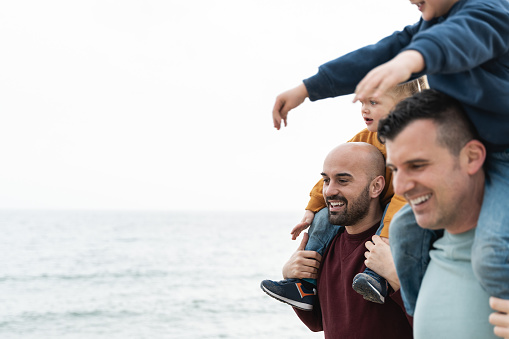 Gay fathers and children playing outdoor on the beach - LGBT family love concept - Soft focus on left dad face
