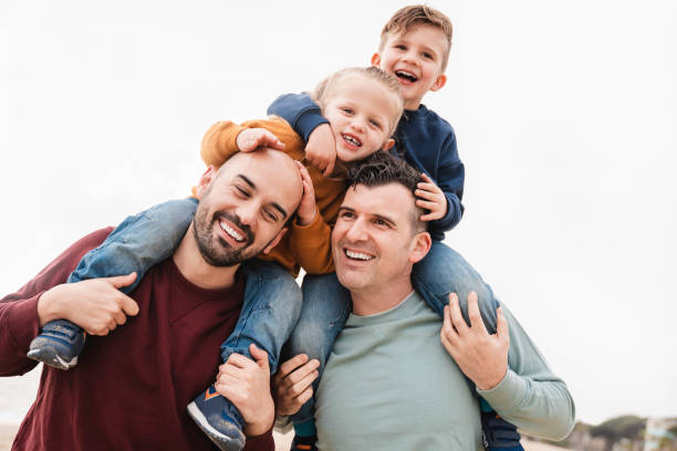Gay fathers and sons playing together outdoor in the city - LGBT family love concept - Focus on right dad face stock photo