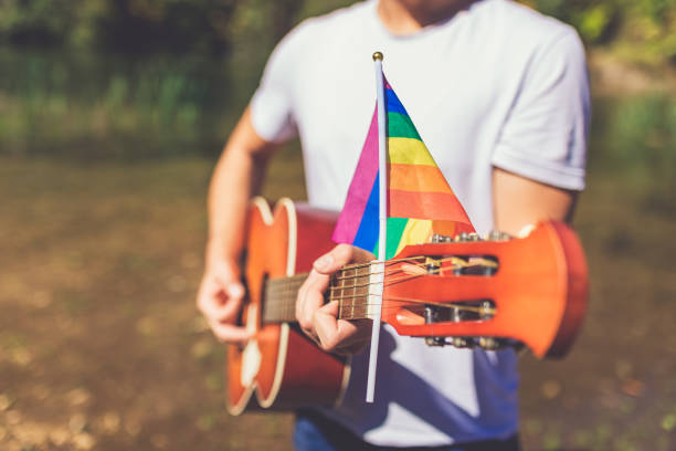Gay guitar player holding acoustic guitar with pride flag outdoors. Space for copy. stock photo