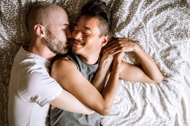 Gay love Directly above of gay partners in bed, lying face to face and, looking each other and cuddling gay spooning stock pictures, royalty-free photos & images