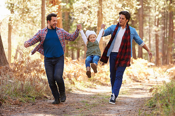 Gay Male Couple With Daughter Walking Through Fall Woodland Gay Male Couple With Daughter Walking Through Fall Woodland gay person stock pictures, royalty-free photos & images