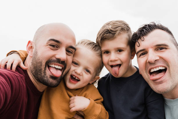 Gay male parents having fun with their sons outdoor in summer day - Lgbt family taking a selfie with smartphone camera - Main focus on left dad face stock photo