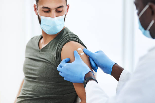 Gearing up for a global scale vaccination Shot of a doctor applying a band aid after injecting a patient in his arm during a consultation at a clinic arm stock pictures, royalty-free photos & images