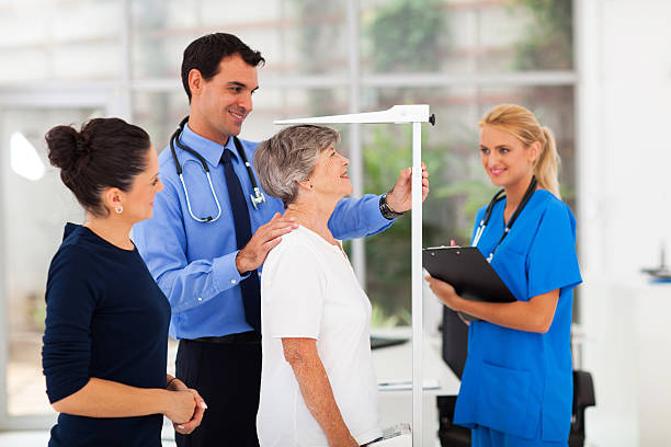 general practitioner measuring senior patient's height stock photo