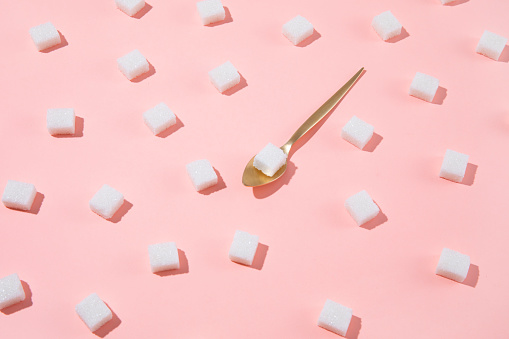 Geometrical pattern with white sugar cubes and a teaspoon on pastel pink background