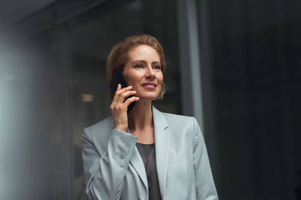 German businesswoman 40-year-old satisfied caucasian businesswoman is standing in office and using smartphone. georgijevic frankfurt stock pictures, royalty-free photos & images