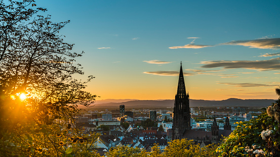 Germany, Freiburg im Breisgau, Magical orange sunset sky and sunrays behind skyline of the beautiful city and muenster