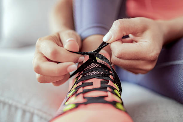 Get ready to run your own life Cropped Image of Young Woman Sitting in Living Room and Tying Shoelaces on Sneakers and Getting Ready for Fitness. Healthy Lifestyle Concept. Running shoes - woman tying shoe laces. Closeup of female sport fitness runner getting ready for jogging. tied up stock pictures, royalty-free photos & images