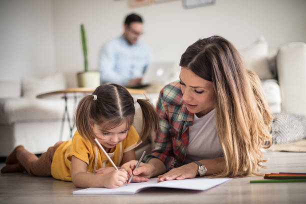 Getting help with my tasks. Getting help with my tasks. Little girl working her homework with mother. Focus is on foreground. home lifestyle stock pictures, royalty-free photos & images