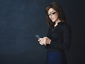 Studio shot of a corporate businesswoman texting on a cellphone against a dark background