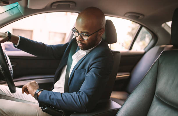 Getting late for work Young african businessman driving a car and checking time. Male driver sitting in car in traffic jam and looking at wristwatch. man driving suit stock pictures, royalty-free photos & images