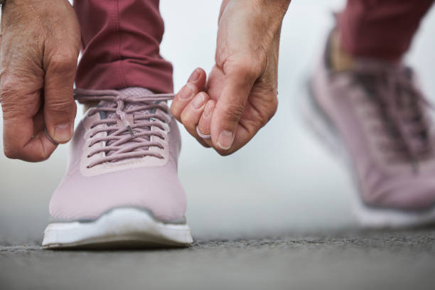 Getting ready Hands of mature sportswoman tying shoelace of right cross-shoe while getting ready for jogging or working out on stadium hands tied up stock pictures, royalty-free photos & images