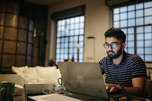 Getting things done from the comfort of home Indian man with eyeglasses sitting at table in apartment and using laptop for working at home indian ethnicity stock pictures, royalty-free photos & images