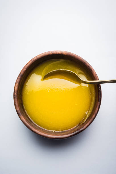 Ghee or clarified butter close up in wooden bowl and silver spoon, selective focus Ghee or clarified butter close up in wooden bowl and silver spoon, selective focus ghee stock pictures, royalty-free photos & images