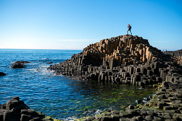 Giant's Causeway in Northern Ireland A woman explores the unique coastline at the Giant's Causeway in Northern Ireland, one of the region's top tourist attractions. basalt column stock pictures, royalty-free photos & images