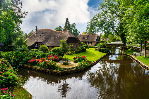 Landscape view of famous Giethoorn village with canals and rustic thatched roof houses in farm area.