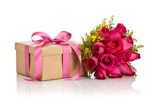 Gift box wrapped with brown craft paper and tied up with pink colored ribbon bow sitting on reflective white background with a roses bouquet. DSRL studio photo taken with Canon EOS 5D Mk II and Canon EF 70-200mm f/2.8L IS II USM Telephoto Zoom Lens