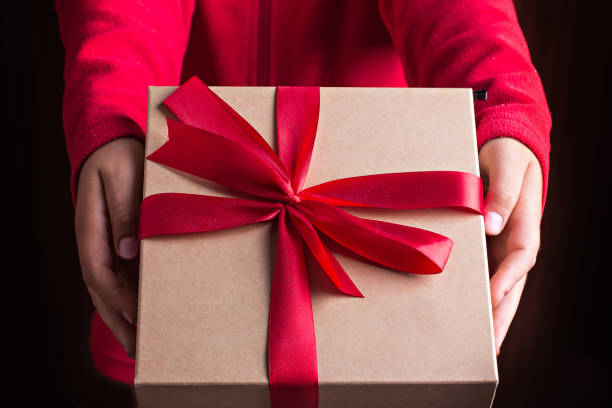 Gift box with a red bow in the hands of a child in a red sweater. stock photo