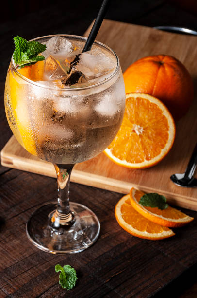gin tonic. alcoholic drink of orange, mint leaves and ice with pieces of fruit on the side. - spot light orange imagens e fotografias de stock