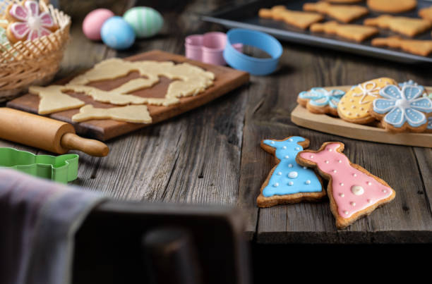 Ginger cookies in the shape of Easter bunny on a wooden table. Process of making Easter cookies from dough. Process of making Easter cookies in the shape of Easter bunny from dough on wooden table. Colorful eggs, a baking sheet with baked cookies and wicker basket with Easter ginger cakes on background. easter sunday stock pictures, royalty-free photos & images