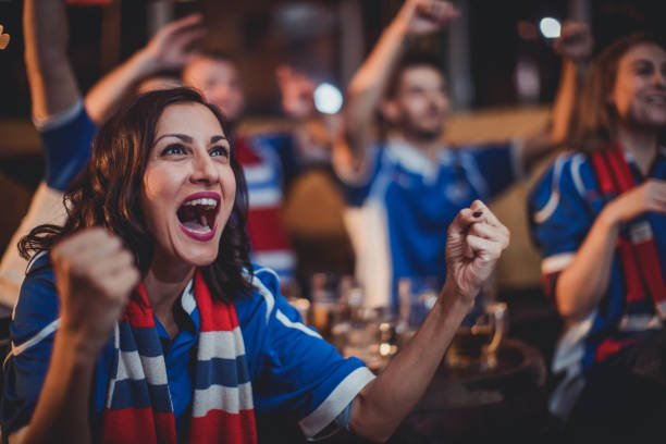 Girl celebrating with friends Group of young people, sitting in a pub all together, watching a sports game. fan enthusiast stock pictures, royalty-free photos & images