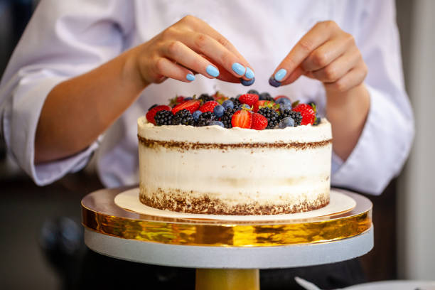 Girl chef cooks confectioner, decorates cake with forest berries. concept making without lactose cakes. Copy space, selective focus stock photo