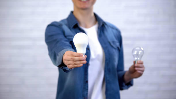 女の子は白熱ランプ、効率の代わりに省エネ導電球を選択します - ハロゲンライト ストックフォトと画像