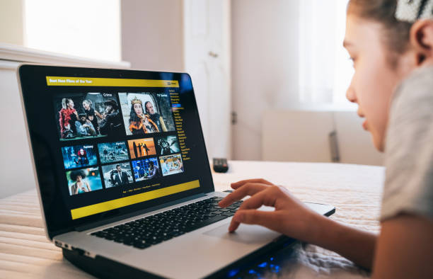 gadis memilih film dan menggunakan laptop di rumah selama isolasi - web film potret stok, foto, & gambar bebas royalti