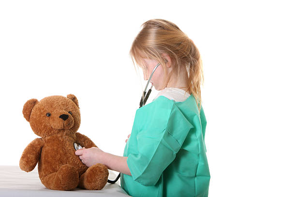 girl doctor listening to teddy bear heart stock photo