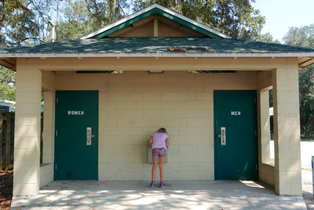 Girl drinking from a water fountain at a public park restroom building stock photo