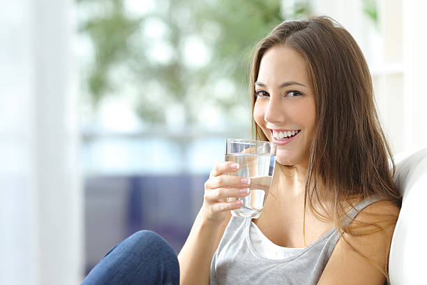 Girl drinking water at home Girl drinking water sitting on a couch at home and looking at camera drinking water stock pictures, royalty-free photos & images