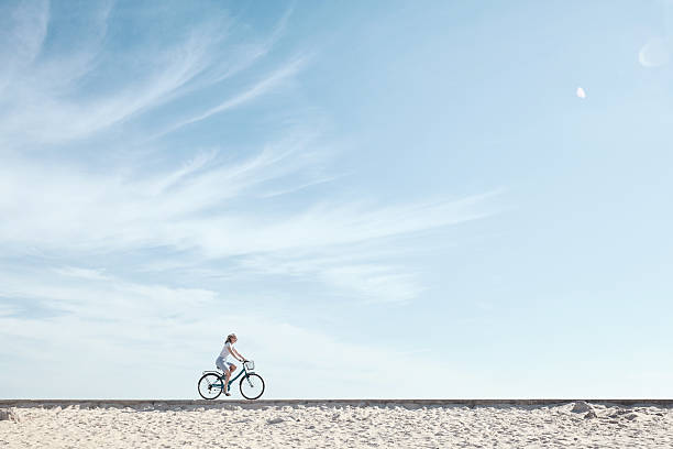 girl enjoying bike ride under sky - fietsen strand stockfoto's en -beelden
