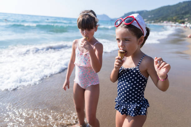 Girl having ice creams when entering the sea Happy children going into the water when eating ice creams little girls in bathing suits stock pictures, royalty-free photos & images