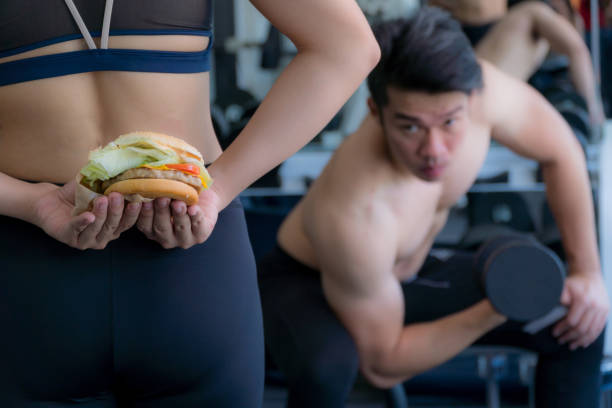 Girl holding a burger secretly behind her.
She will bring a burger to her boyfriend as a gift after a hard workout.
Concept for health. stock photo