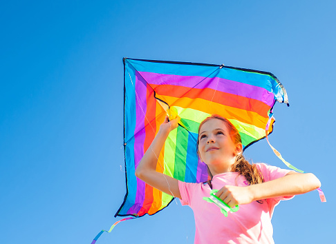 Child girl portrait with rainbow kite on blue sky background