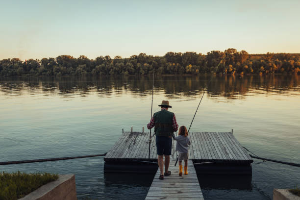 Girl holding grandfather's hand and going fishing on the deck stock photo