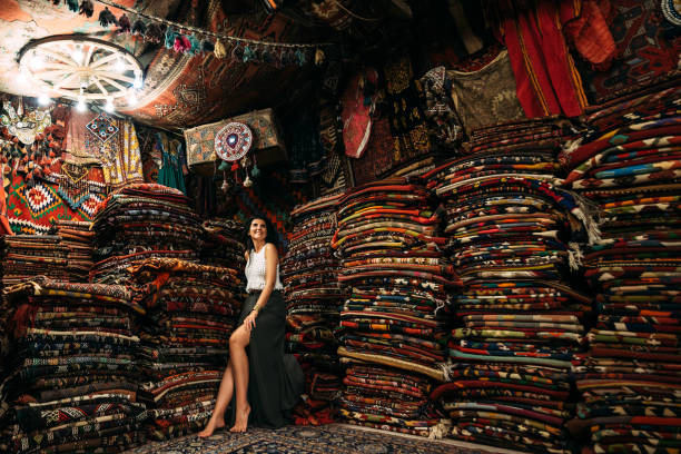 Chica en una tienda de alfombras. Una clienta feliz eligiendo alfombras de colores en una tienda de alfombras. Chica en el mercado turco con asombrosas alfombras de colores. Alegre mujer cliente compras alfombra en interior tienda alfombras fotografías e imágenes de stock