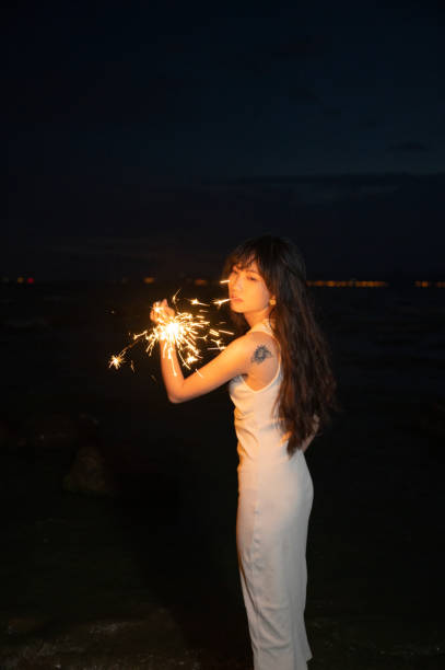 A girl in a fashionable white dress plays with a lamp by the sea stock photo
