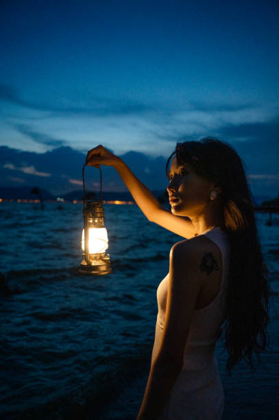 A girl in a fashionable white dress plays with a lamp by the sea stock photo