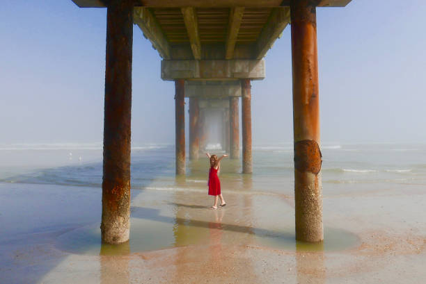 Girl in a red dress under a beach pier stock photo