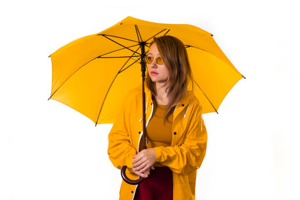 A girl in a yellow raincoat and glasses stands under an umbrella. Isolate on white background stock photo