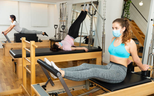 Girl in protective mask practicing pilates on reformer at gym stock photo
