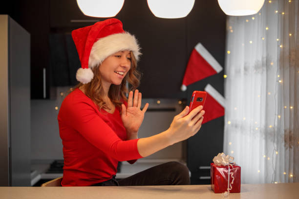 A girl in red clothes in the kitchen looks into a smartphone on christmas eve stock photo