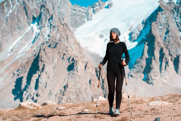 Girl is hiking in the snowy mountains. A young beautiful sports girl in thermal underwear with trekking poles walks along the trail among the snow-capped high peaks of the mountains, the traveler walks and climbs tin the national park. tien shan mountains stock pictures, royalty-free photos & images