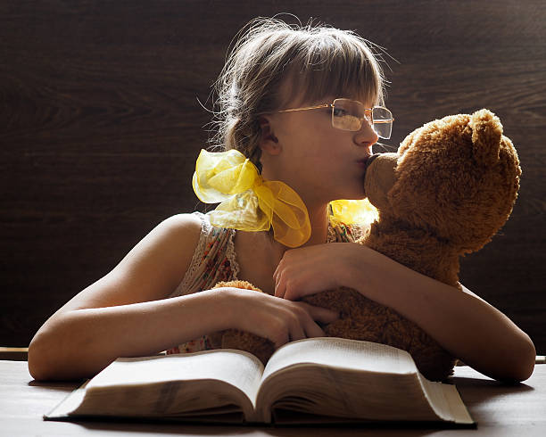 Girl kissing teddy bear Girl kissing teddy bear. Portrait of a child with a toy. Sunlight. The girl has bright yellow bows. Girl schoolgirl teenager. Before an open book child teddy ray stock pictures, royalty-free photos & images
